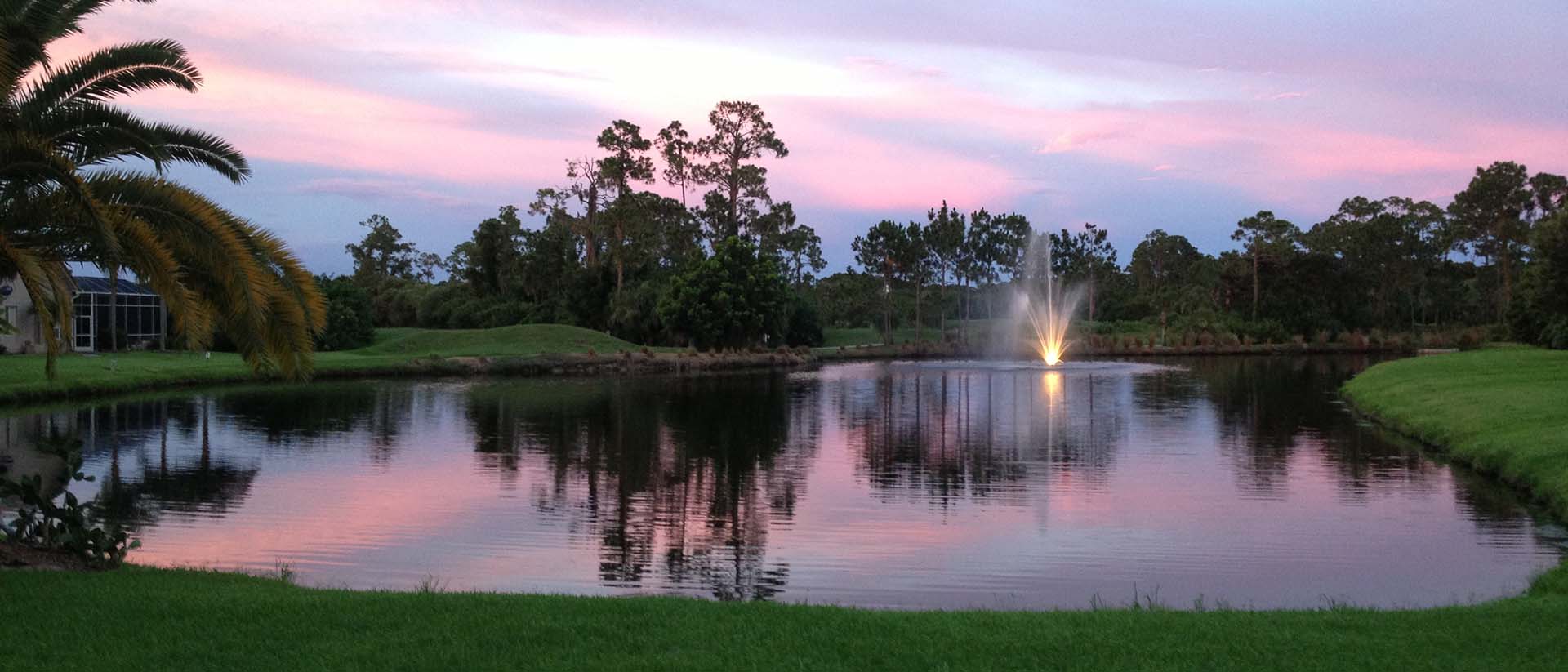 pond with fountain against a pink and purple sunset